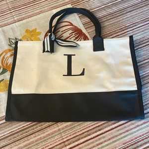 Black and tan canvas tote bag with embroidered “L” in black